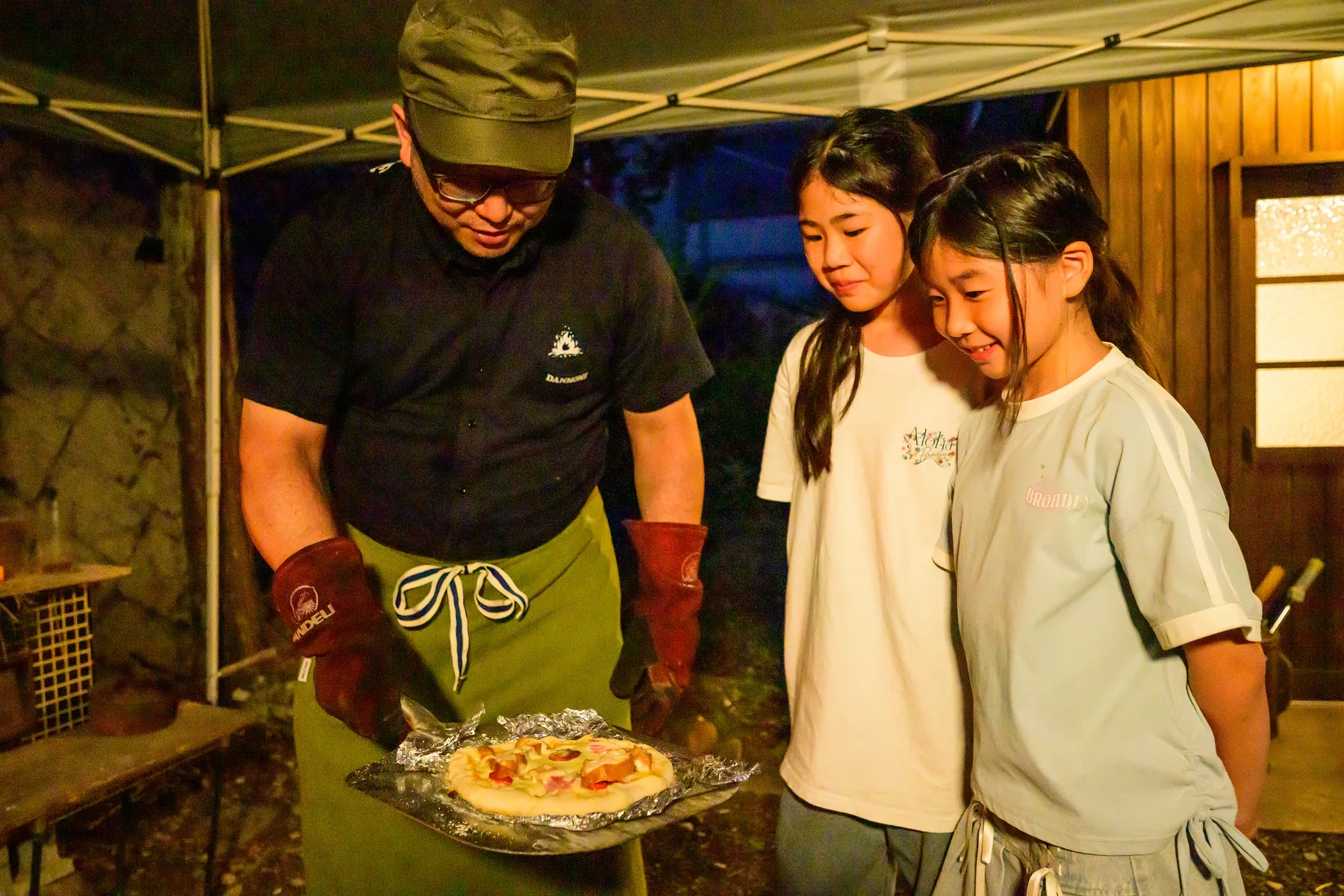 焼き上がったピザを持つ男性と、それを見る子どもたち