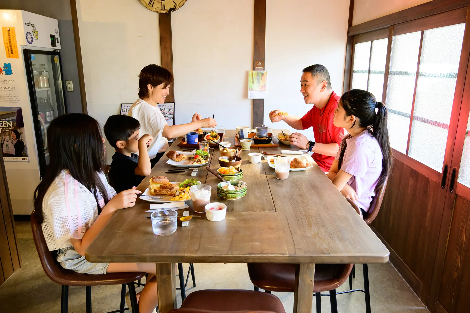 古民家カフェの長いテーブルで食事と会話を楽しむ家族